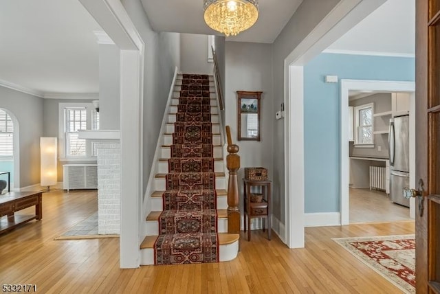 stairs with ornamental molding, wood-type flooring, and a notable chandelier