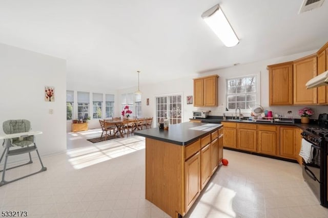 kitchen with black range oven, sink, a kitchen island, and decorative light fixtures