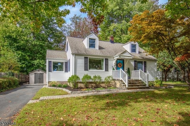 cape cod home featuring a front lawn and a storage unit