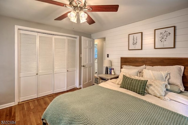 bedroom featuring ceiling fan, wooden walls, a closet, and wood-type flooring