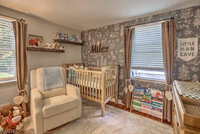 bedroom with a crib, wood-type flooring, and multiple windows