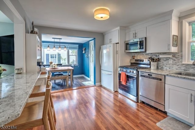 kitchen featuring stainless steel appliances, decorative light fixtures, white cabinetry, light stone counters, and hardwood / wood-style flooring