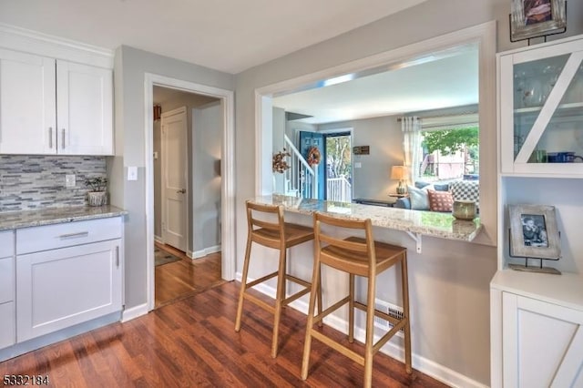 kitchen featuring light stone countertops, a breakfast bar, dark hardwood / wood-style flooring, white cabinets, and tasteful backsplash