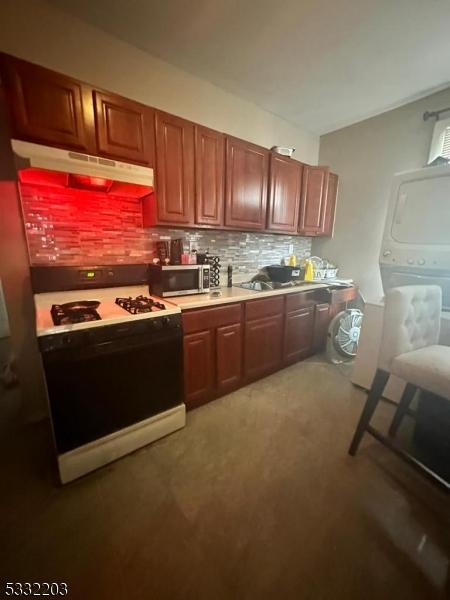 kitchen featuring backsplash, sink, white range oven, and stacked washer / dryer