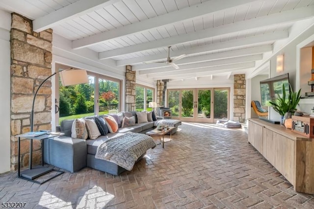 sunroom featuring beam ceiling, ceiling fan, a wood stove, and a healthy amount of sunlight