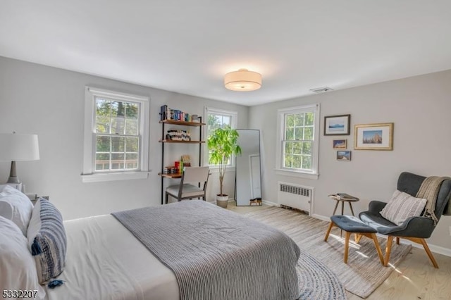 bedroom with multiple windows, light wood-type flooring, and radiator heating unit