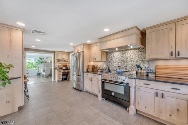 kitchen featuring stainless steel appliances, custom range hood, light brown cabinets, and tasteful backsplash