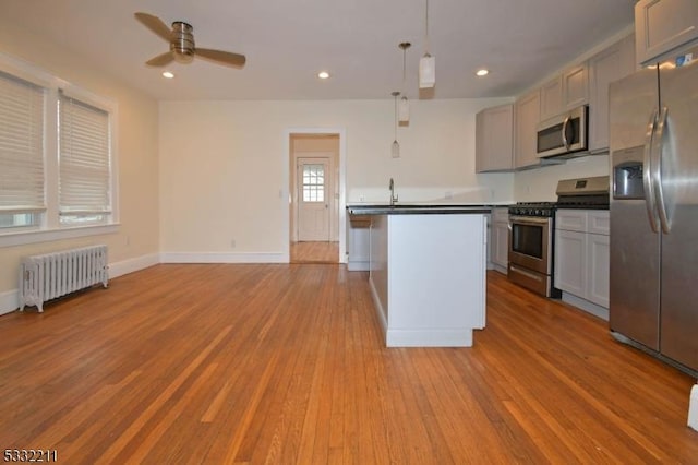 kitchen featuring ceiling fan, appliances with stainless steel finishes, gray cabinetry, decorative light fixtures, and radiator