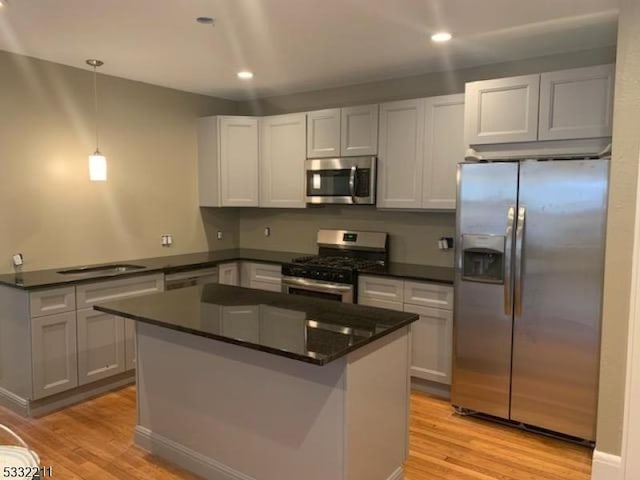 kitchen with decorative light fixtures, light wood-type flooring, stainless steel appliances, and a center island