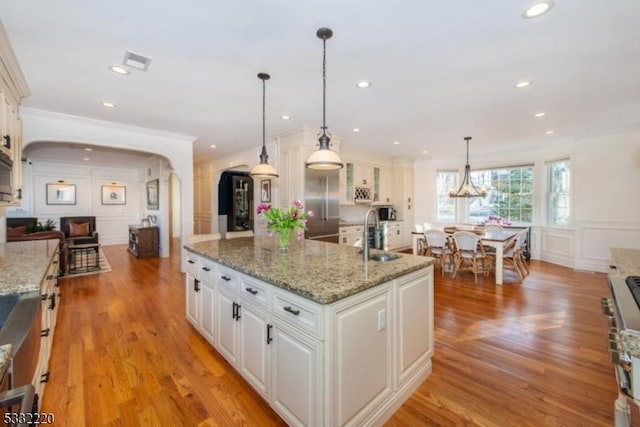 kitchen featuring white cabinetry, a center island with sink, hanging light fixtures, light stone countertops, and sink