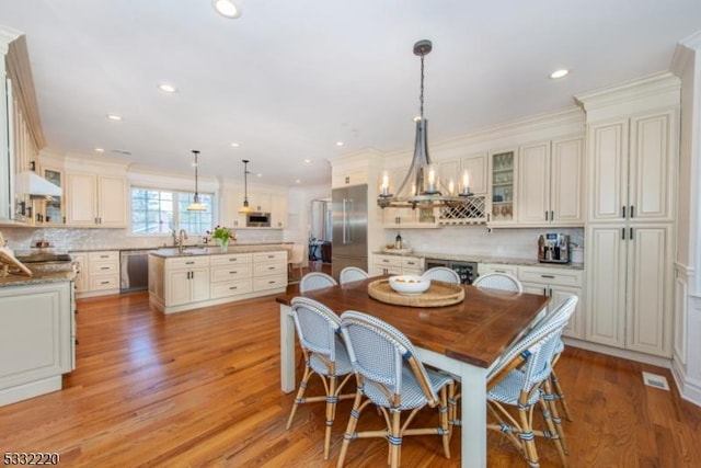 dining space featuring light wood-type flooring, ornamental molding, a notable chandelier, and sink