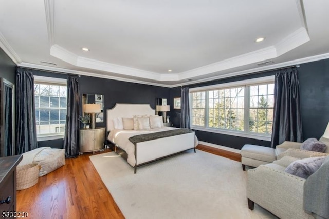 bedroom with hardwood / wood-style flooring, crown molding, and a raised ceiling