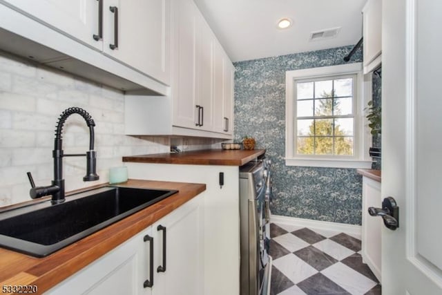 kitchen featuring white cabinets, butcher block countertops, sink, and washer / dryer