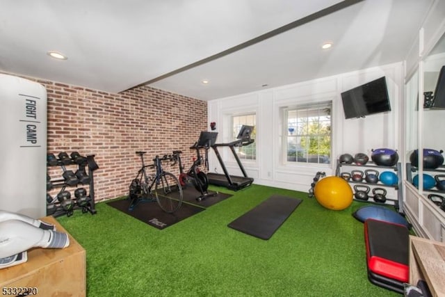 exercise area featuring brick wall, golf simulator, and carpet flooring