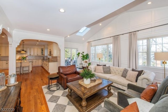 living room featuring a wealth of natural light, vaulted ceiling, ornamental molding, and light wood-type flooring