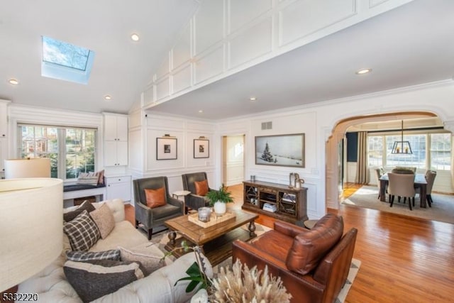 living room featuring high vaulted ceiling, a skylight, crown molding, and light hardwood / wood-style flooring