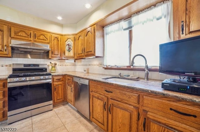 kitchen with stainless steel appliances, sink, light stone counters, wall chimney exhaust hood, and light tile patterned floors