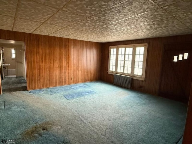 carpeted spare room with radiator and wood walls