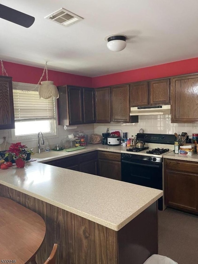 kitchen featuring kitchen peninsula, decorative light fixtures, a kitchen breakfast bar, dark brown cabinets, and gas range oven