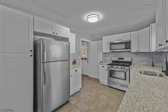 kitchen featuring white cabinets, appliances with stainless steel finishes, light stone countertops, and sink