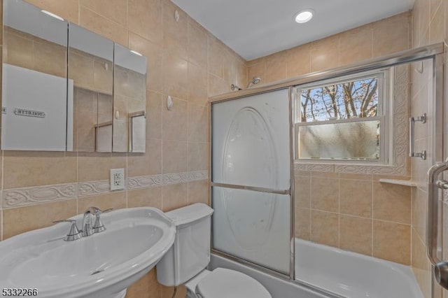 full bathroom with toilet, shower / bath combination with glass door, sink, and tile walls