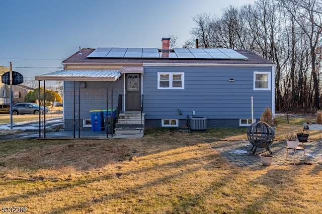 back of property with central AC unit, solar panels, a yard, and an outdoor fire pit