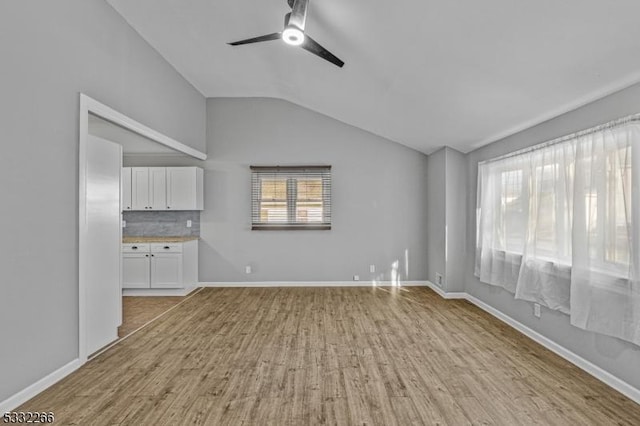 unfurnished living room featuring light hardwood / wood-style flooring, vaulted ceiling, ceiling fan, and a healthy amount of sunlight