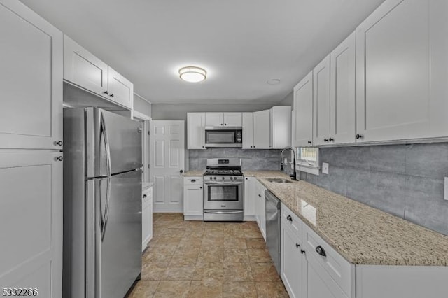 kitchen with sink, light stone counters, backsplash, white cabinets, and appliances with stainless steel finishes