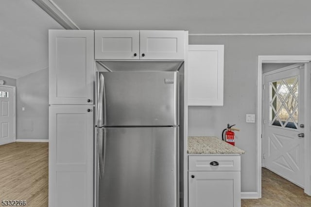 kitchen with white cabinets, light stone counters, and stainless steel refrigerator