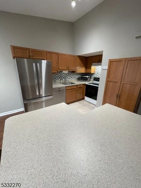 kitchen featuring backsplash, a high ceiling, sink, light hardwood / wood-style flooring, and stainless steel appliances