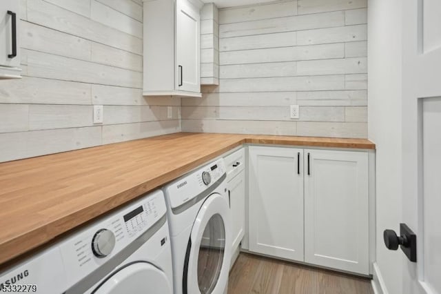 clothes washing area with light hardwood / wood-style floors, cabinets, wood walls, and washing machine and dryer