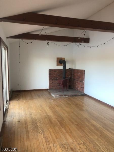 unfurnished living room with hardwood / wood-style flooring, vaulted ceiling with beams, and a wood stove