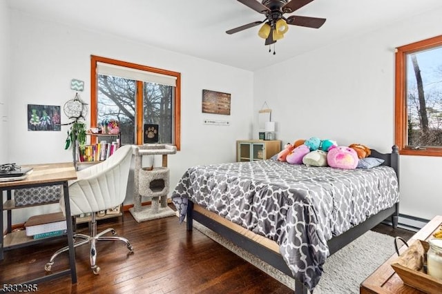 bedroom with ceiling fan, a baseboard heating unit, dark wood-type flooring, and multiple windows