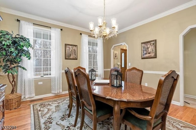 dining space with light wood-type flooring, an inviting chandelier, and crown molding