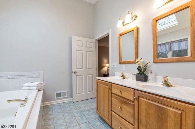 bathroom with vanity, tile patterned flooring, a skylight, and tiled bath