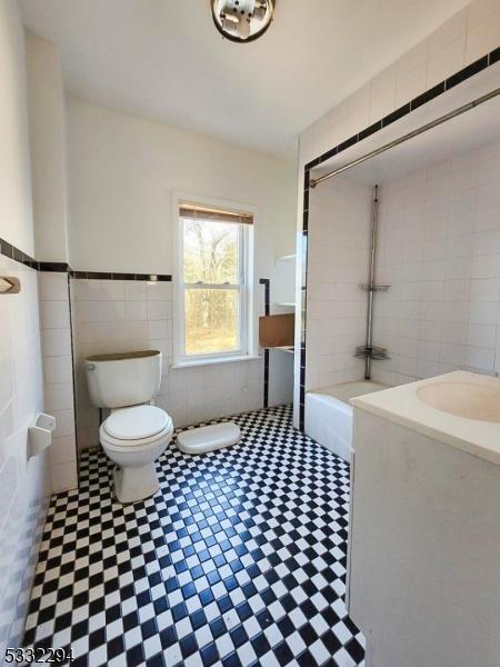 bathroom with a bathtub, toilet, tile walls, and sink