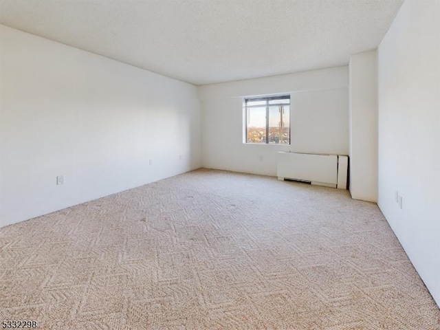 unfurnished room featuring radiator heating unit and light carpet