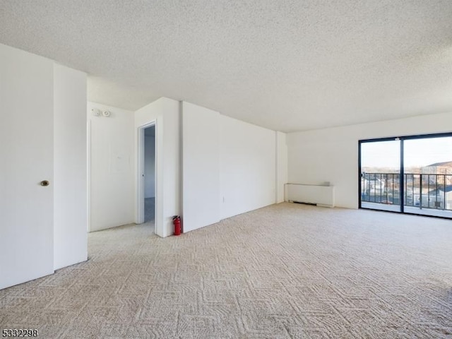 unfurnished room with radiator, light carpet, and a textured ceiling