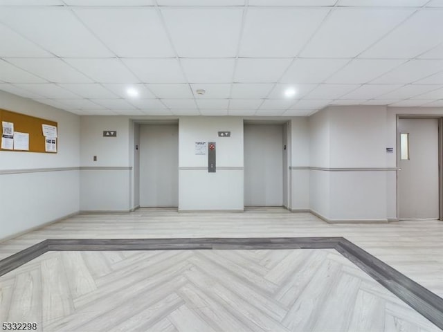 unfurnished room with light parquet flooring, elevator, and a drop ceiling