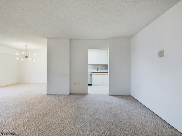 empty room featuring sink, light carpet, a textured ceiling, and a chandelier