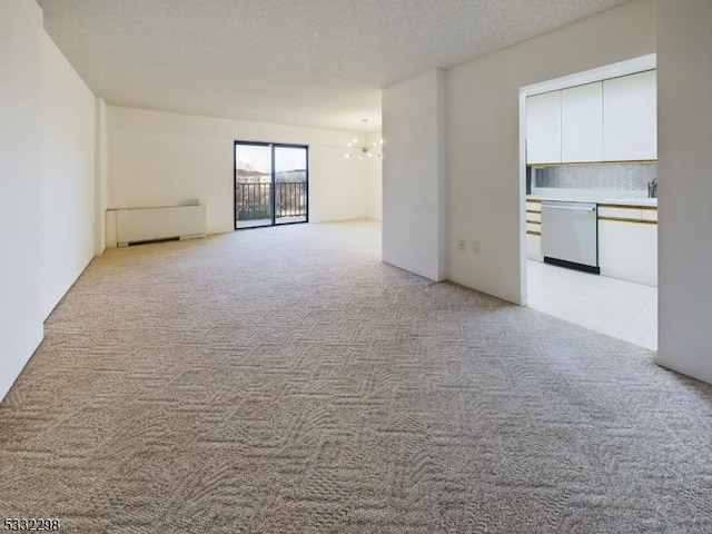 carpeted empty room with an inviting chandelier, radiator, and a textured ceiling