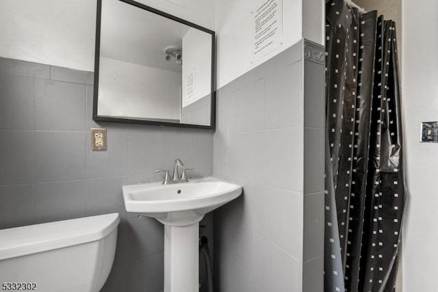 bathroom with tile walls, toilet, a shower with curtain, and sink