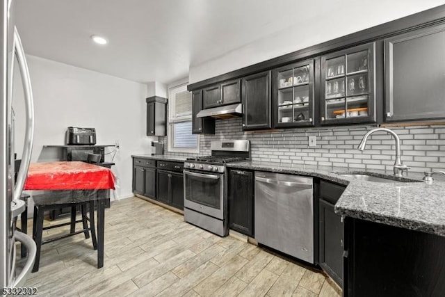 kitchen featuring dark stone countertops, appliances with stainless steel finishes, light hardwood / wood-style floors, sink, and backsplash