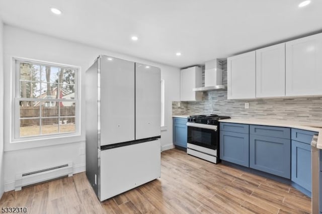 kitchen featuring wall chimney exhaust hood, a baseboard radiator, white refrigerator, range with gas stovetop, and white cabinets