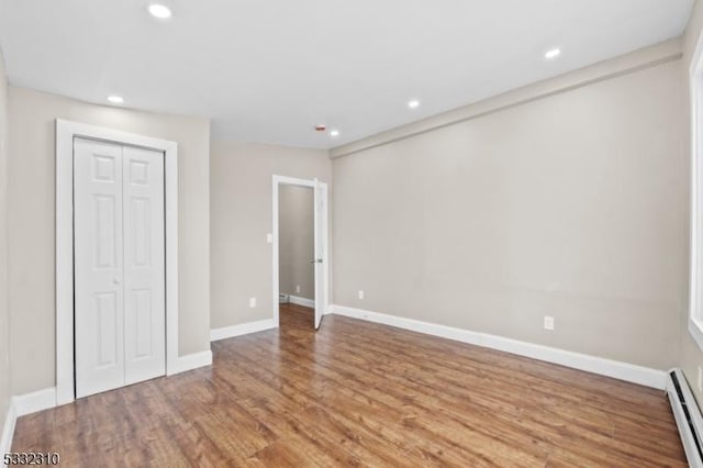 unfurnished bedroom with a closet, a baseboard radiator, and hardwood / wood-style flooring