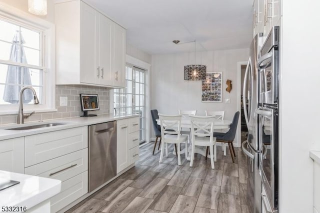 kitchen with dishwasher, sink, white cabinets, backsplash, and hanging light fixtures