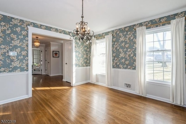 unfurnished dining area with hardwood / wood-style flooring, ornamental molding, a wealth of natural light, and an inviting chandelier