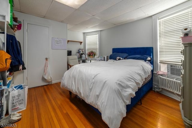 bedroom with a paneled ceiling, wood-type flooring, radiator heating unit, and multiple windows