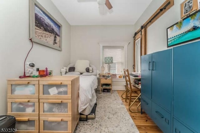 bedroom with ceiling fan, a barn door, and light wood-type flooring