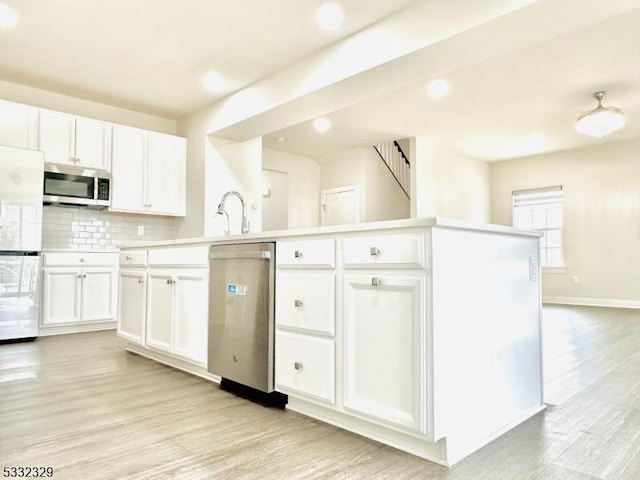 kitchen featuring stainless steel appliances, white cabinetry, tasteful backsplash, and an island with sink